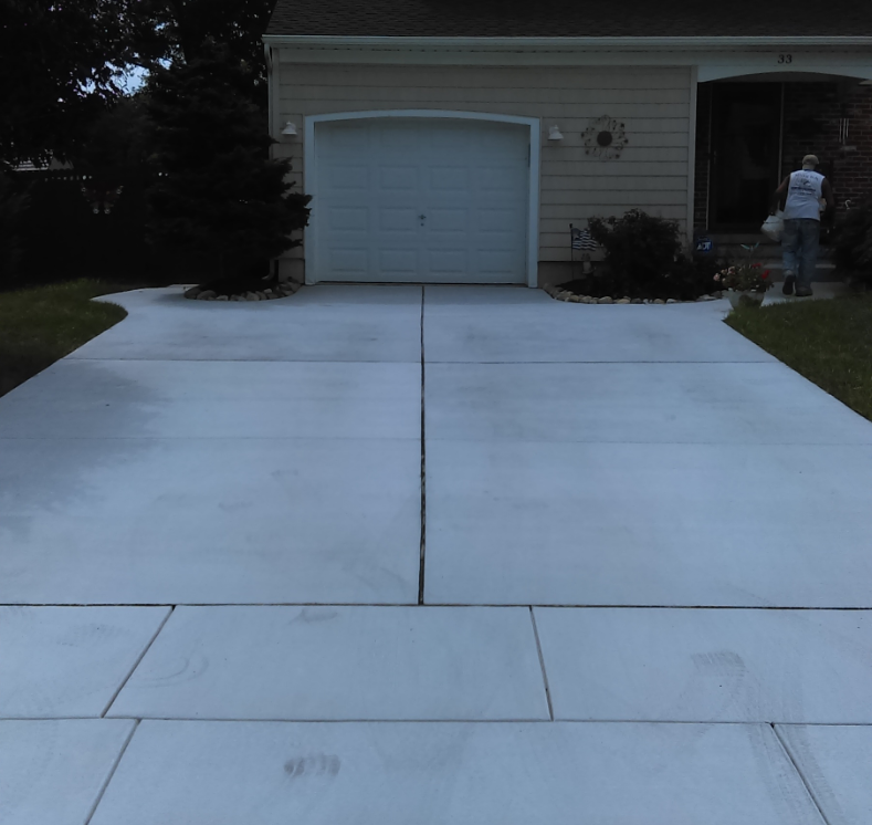 Concrete driveway leading to a garage door. A person stands near the front door.