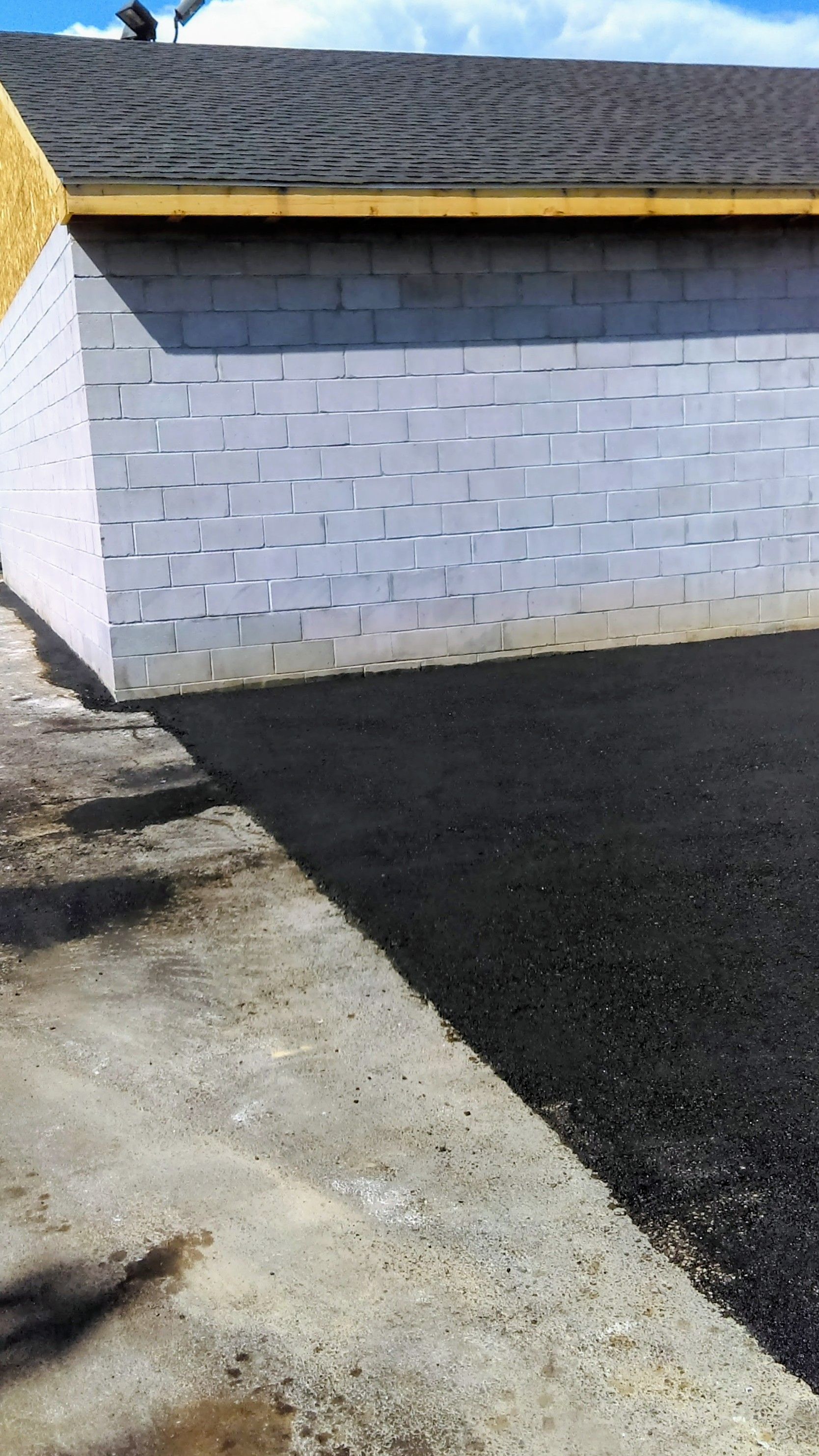 Gray cinder block wall with asphalt and concrete surfaces; blue sky.