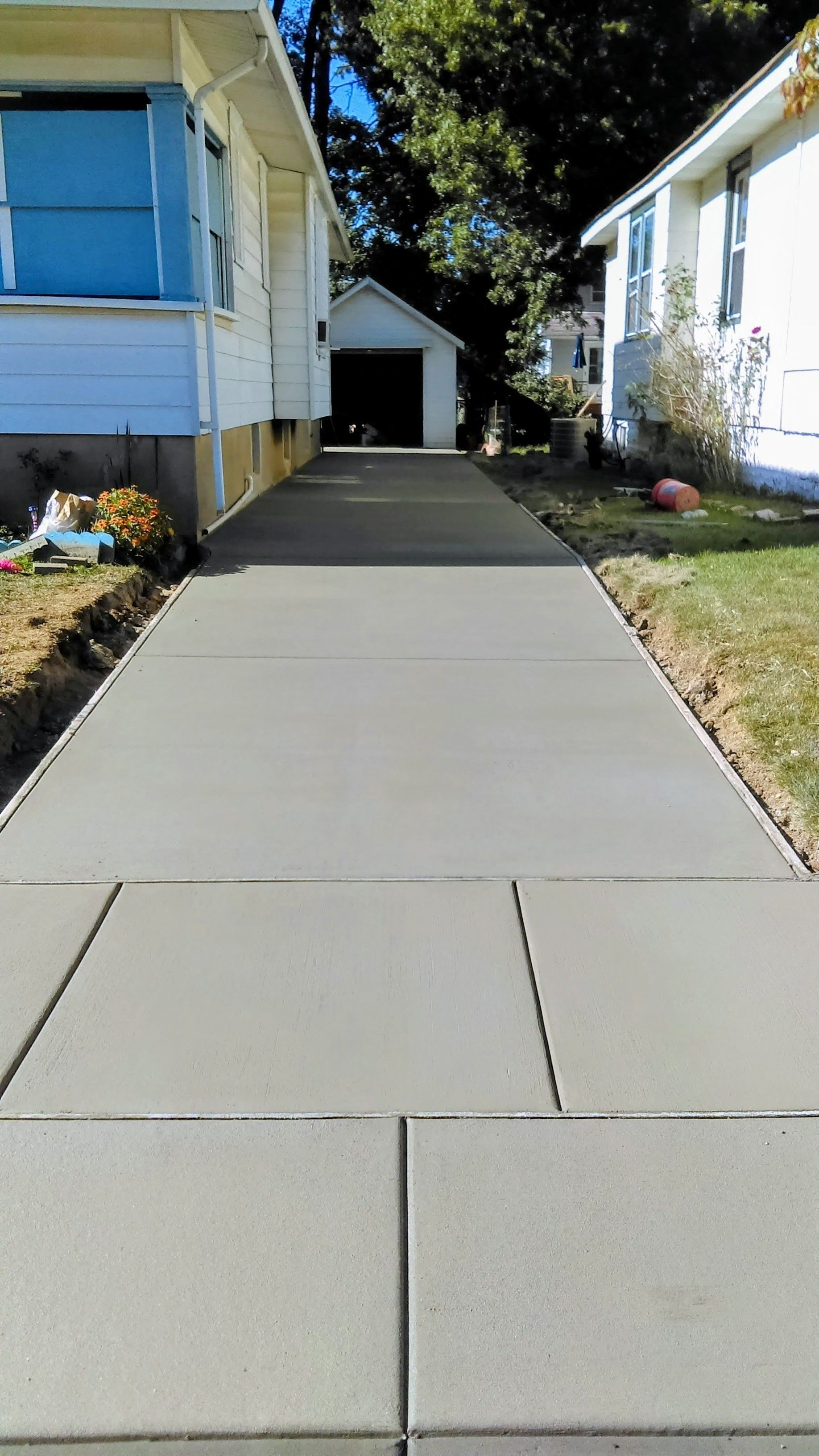 Newly poured concrete driveway between two houses, leading to a detached garage.