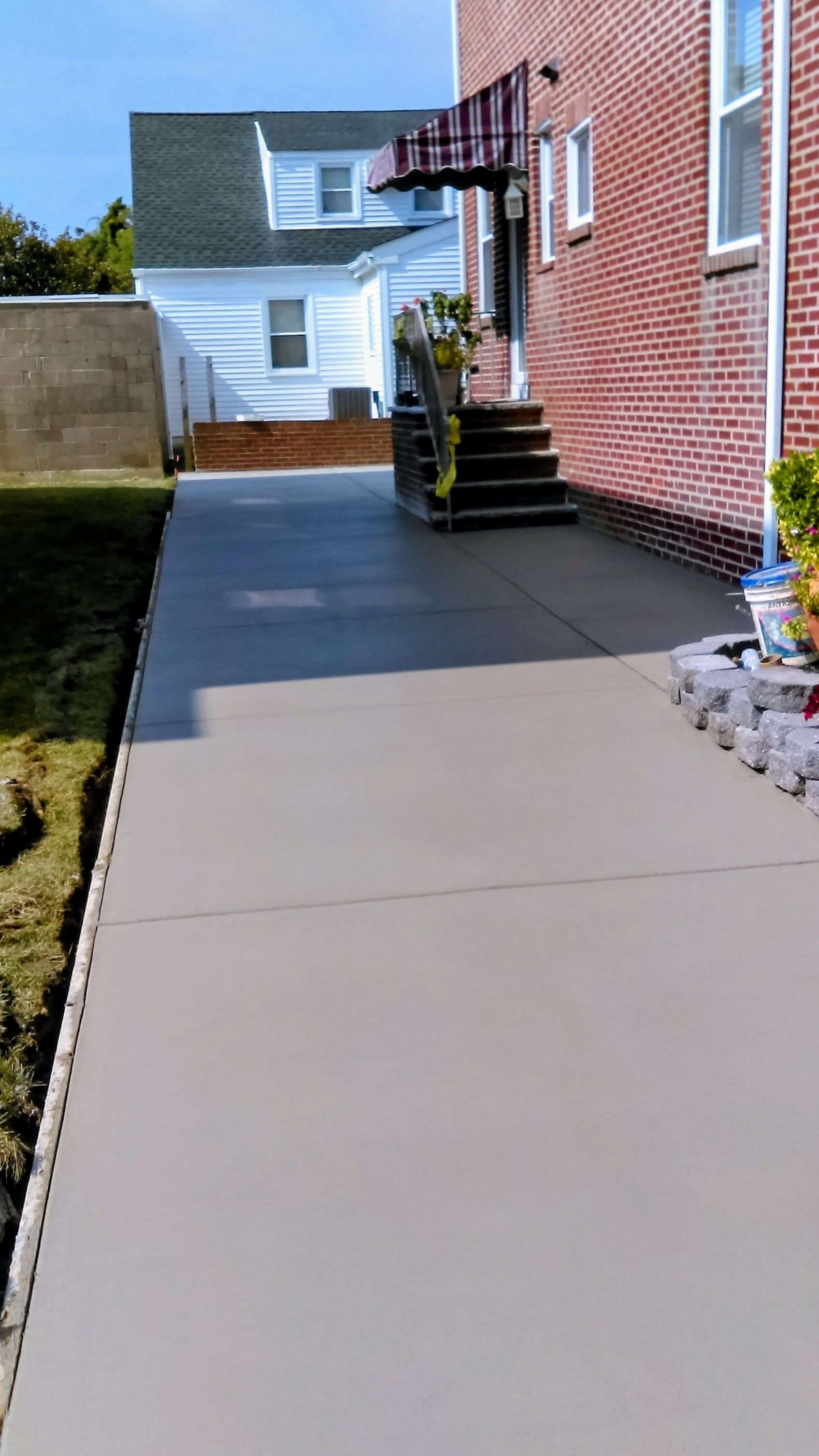 Newly poured concrete sidewalk next to a brick building, leading to stairs. Sunny day.