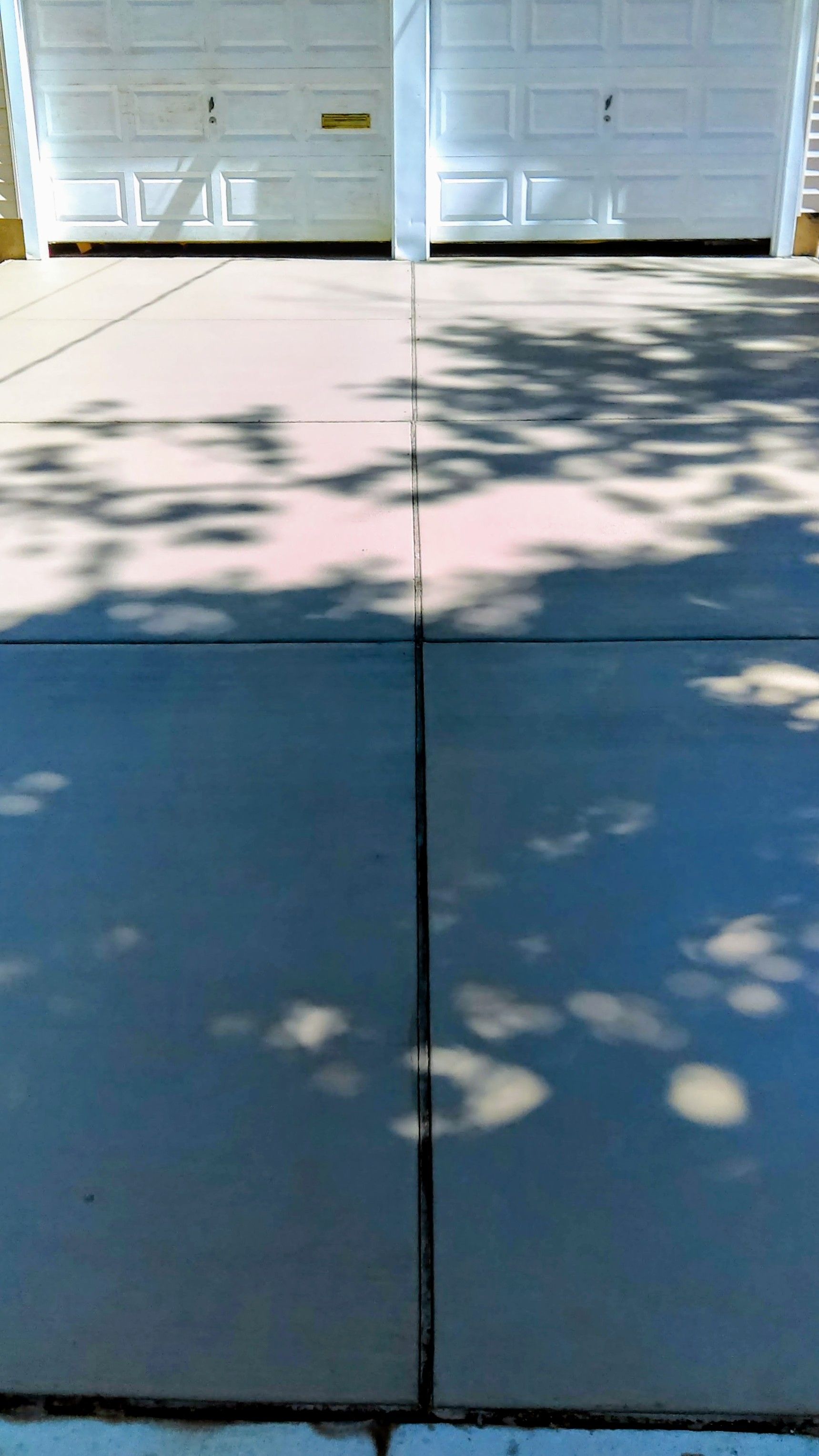 Driveway with two white garage doors; shadows of trees cast across the concrete.