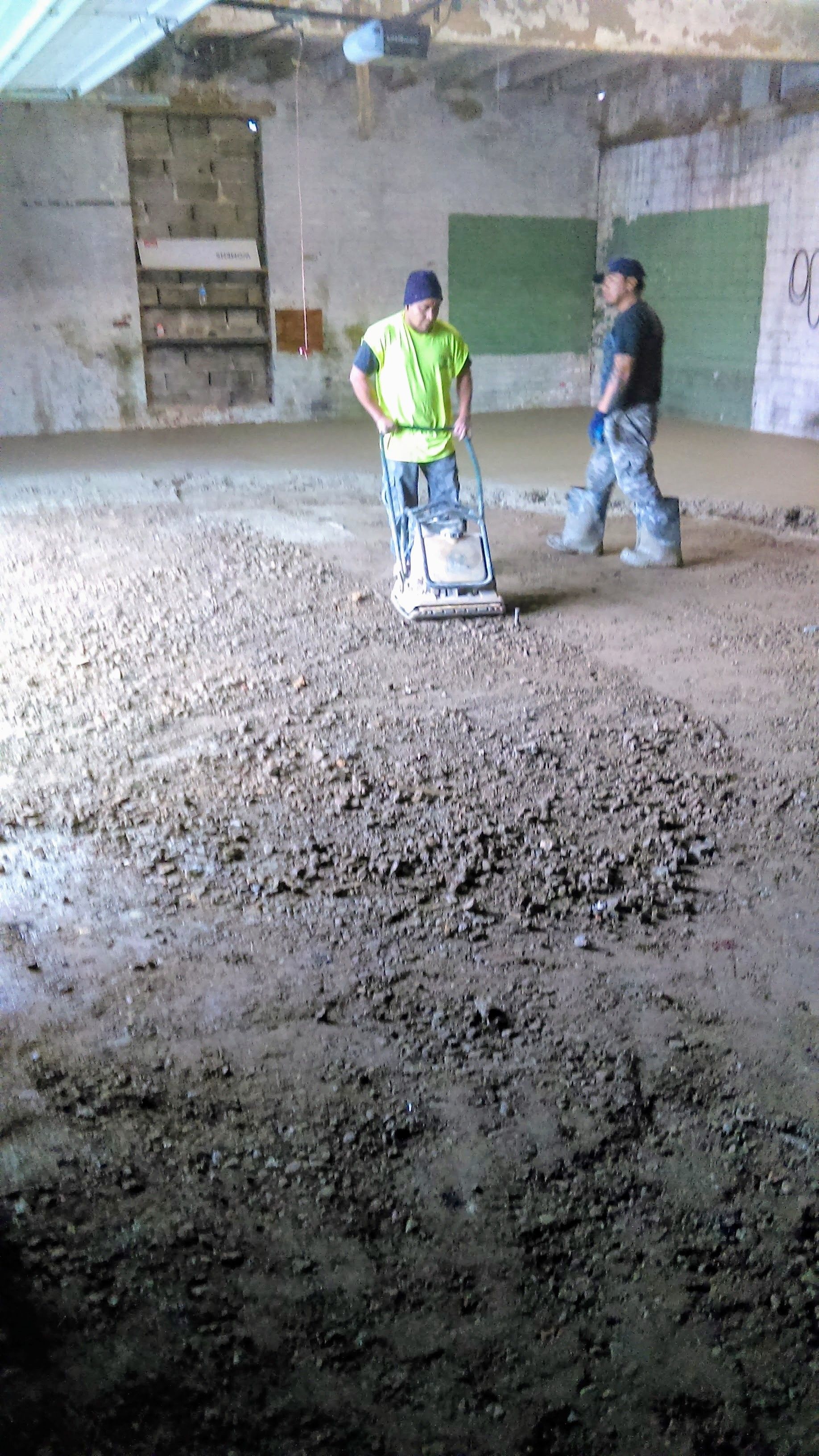 Two workers smoothing concrete floor in a building using a vibrating machine.