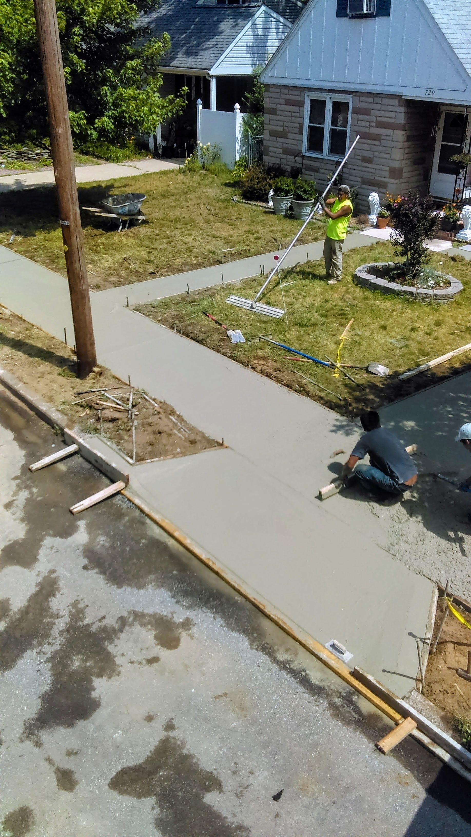 Concrete sidewalk being poured by construction workers near a house on a sunny day.