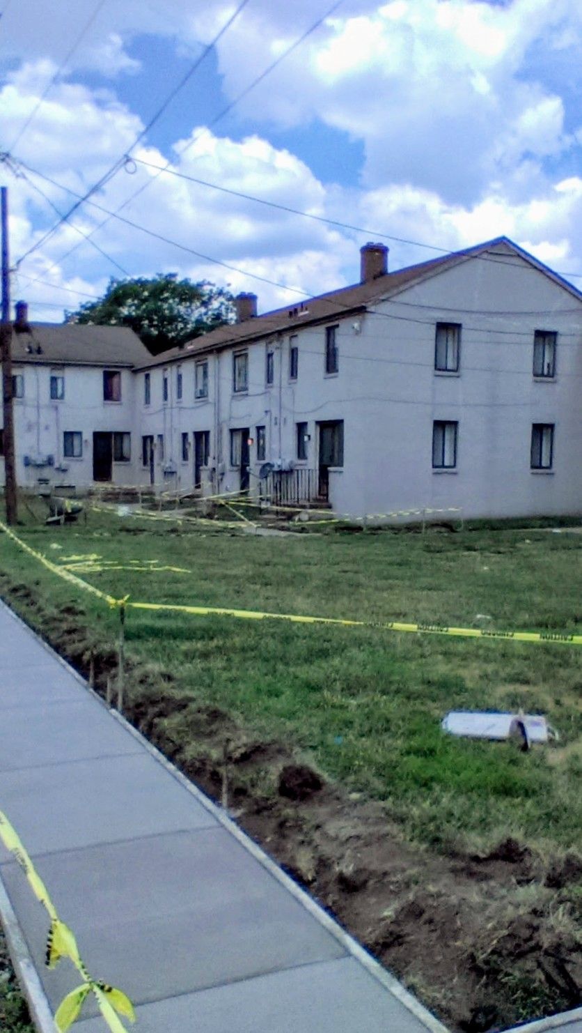 Row of light-colored townhouses with a grassy yard, construction underway along the sidewalk.