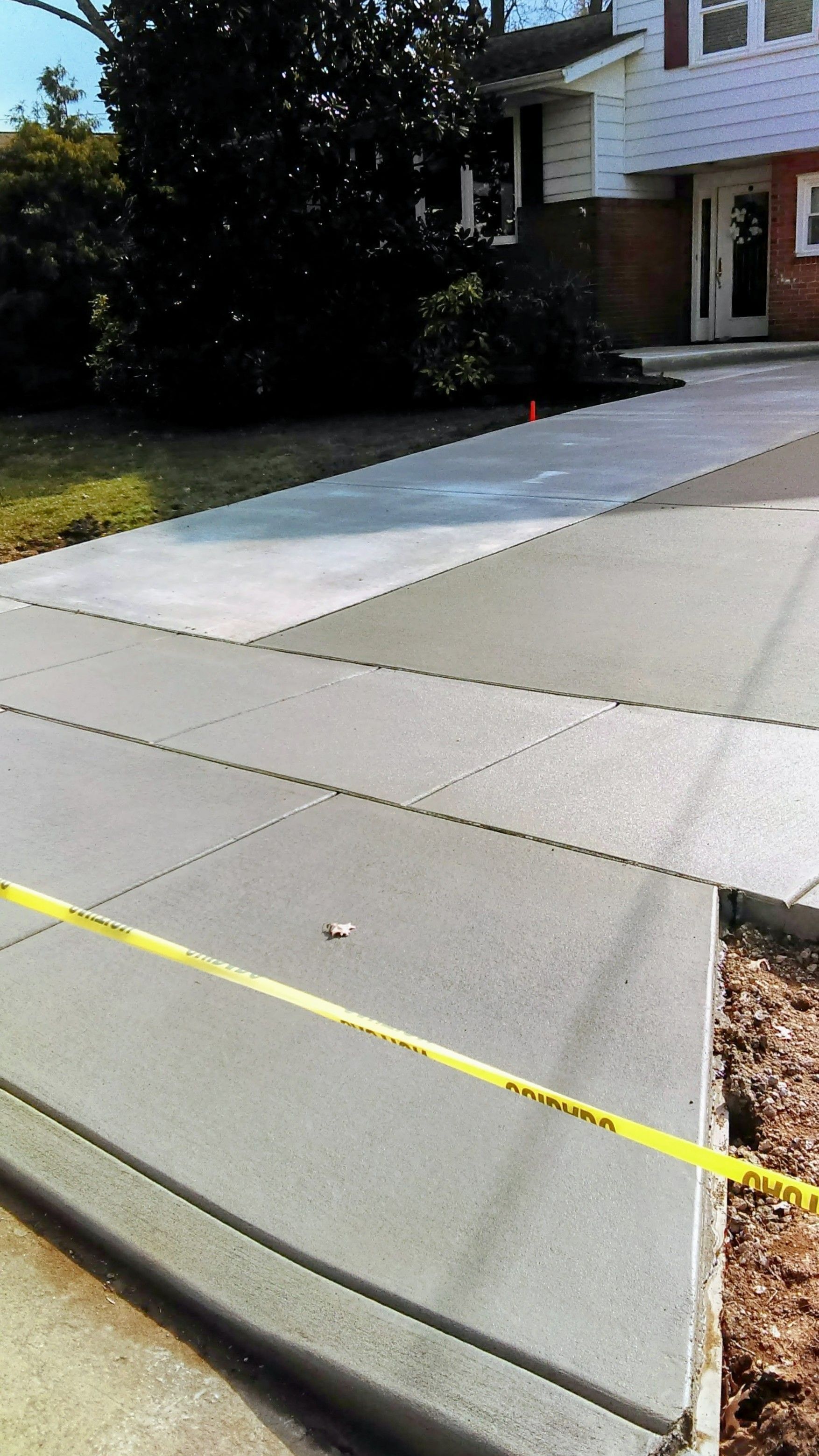 Newly poured concrete driveway with yellow caution tape, leading to a house.