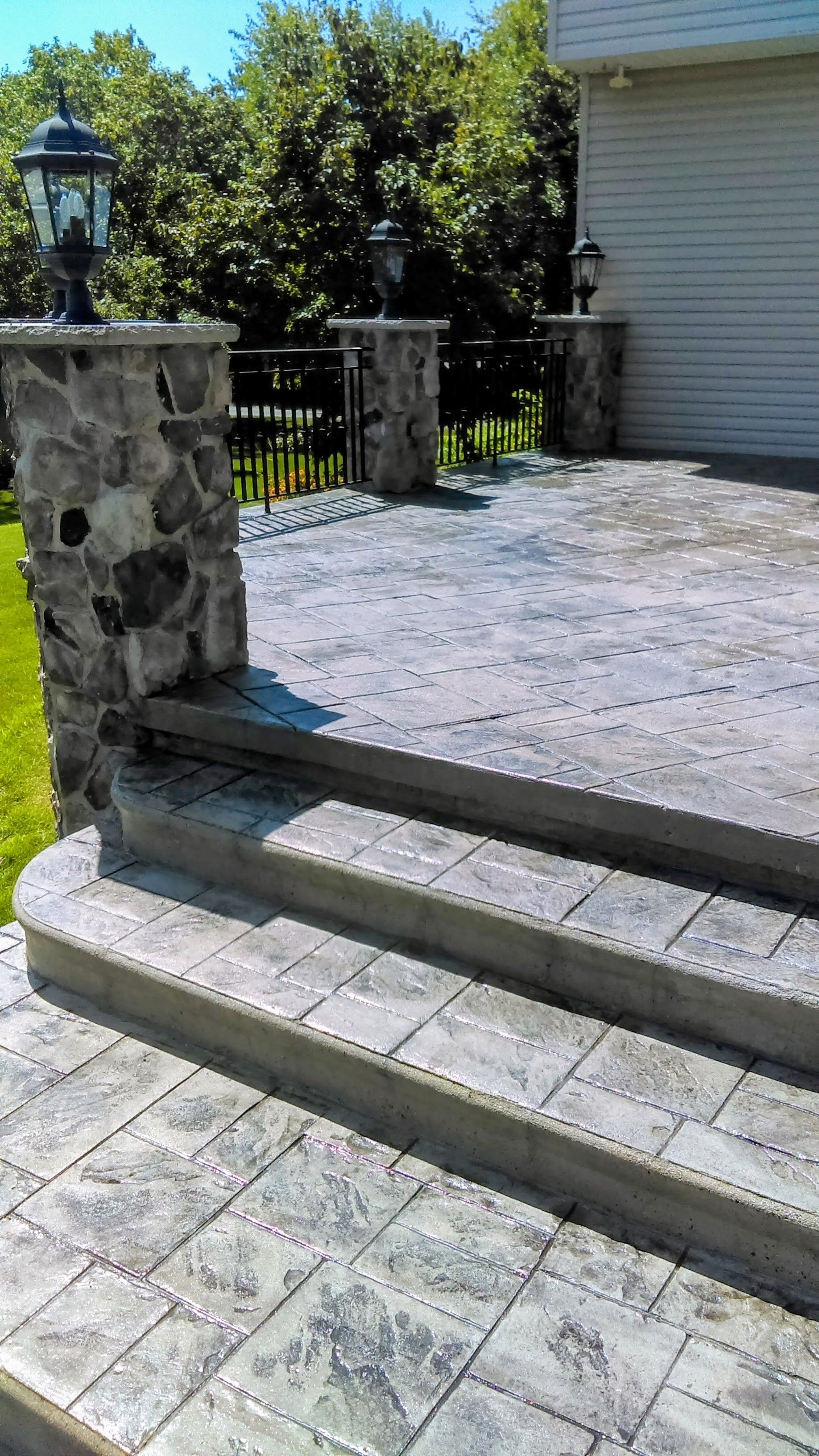 Stone patio with steps and pillars, featuring decorative lamps.