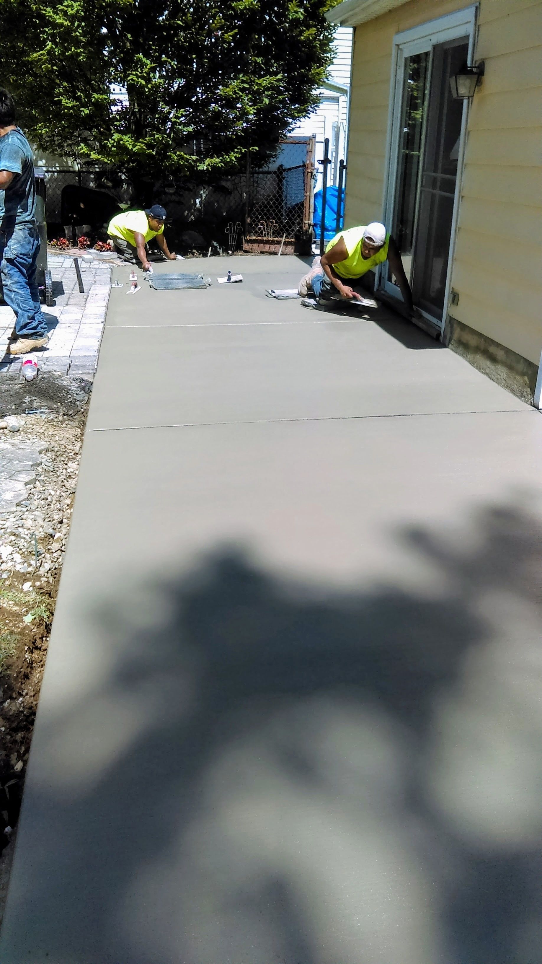 Workers smoothing wet concrete for a sidewalk next to a building.