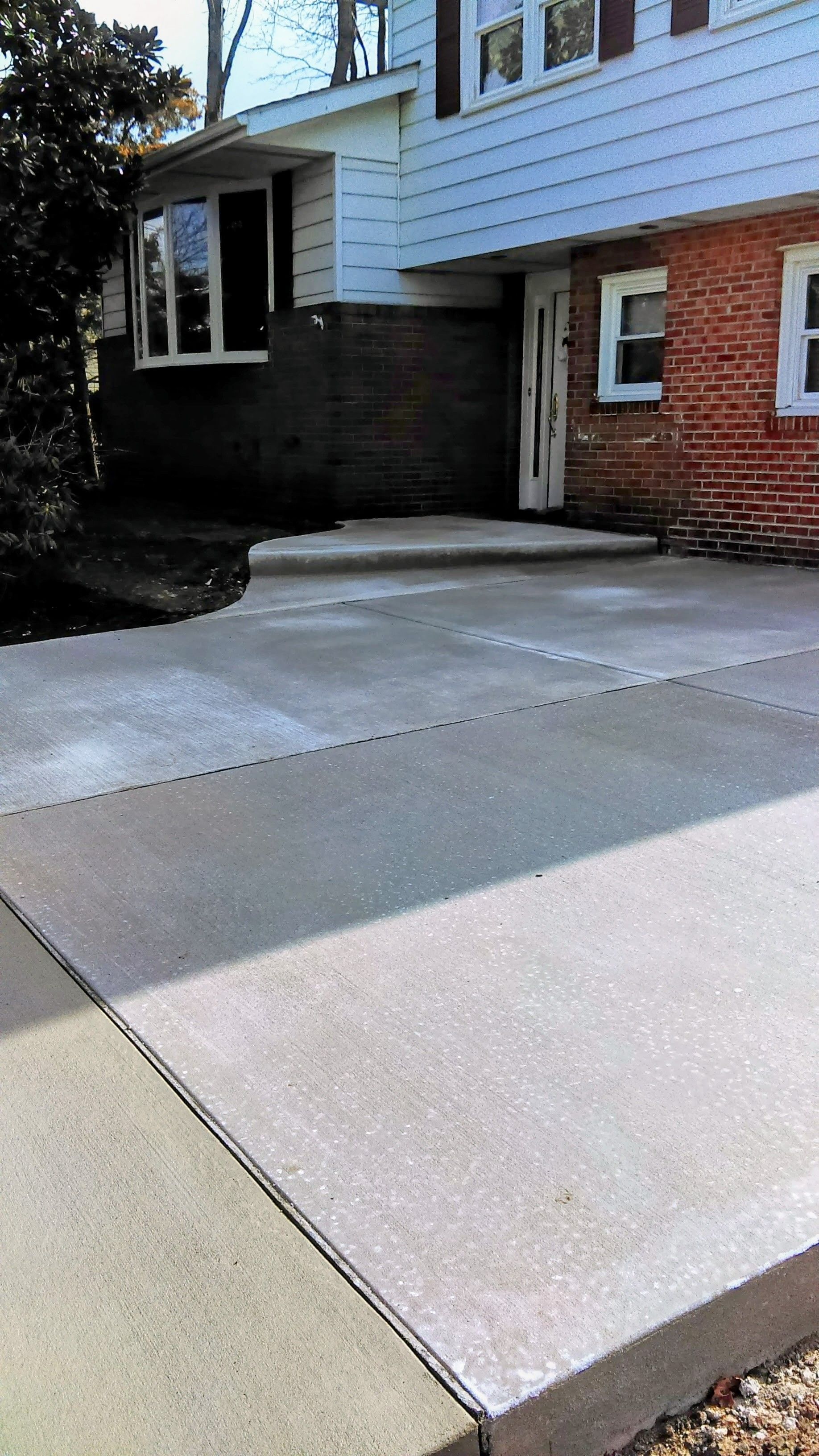 Concrete driveway leading to a two-story house with brick and siding.