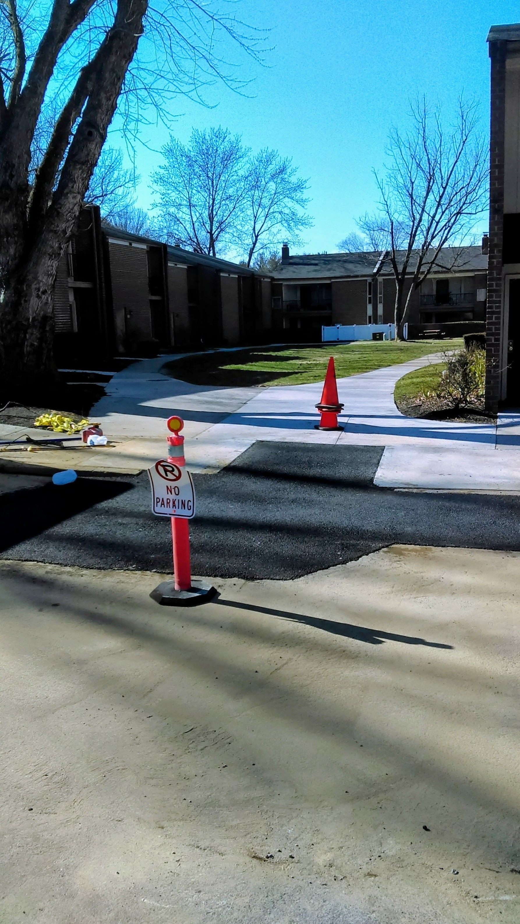 Asphalt repair area with orange traffic cones in front of apartment buildings on a sunny day.