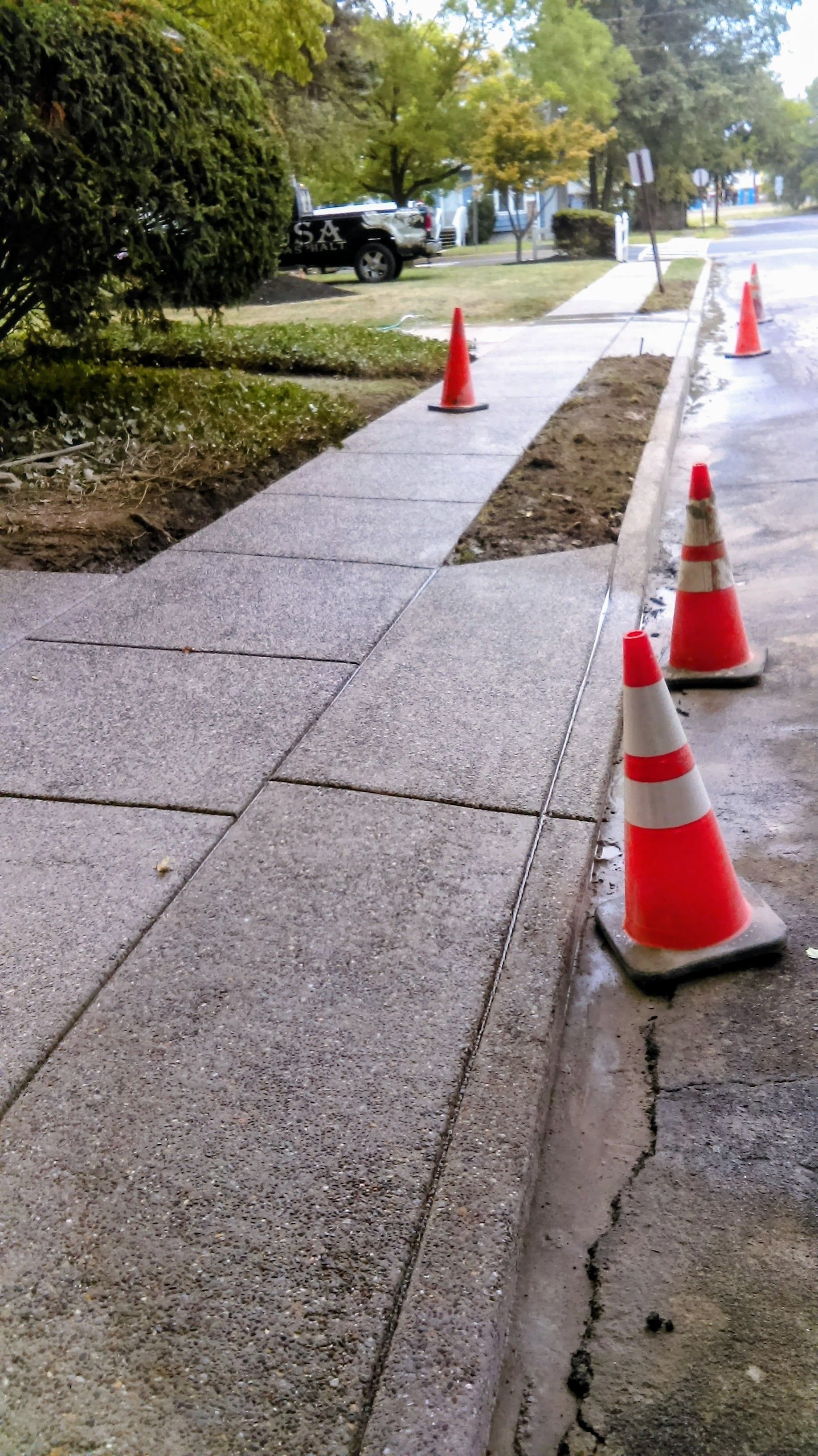 Sidewalk with orange traffic cones, curb repair in progress.