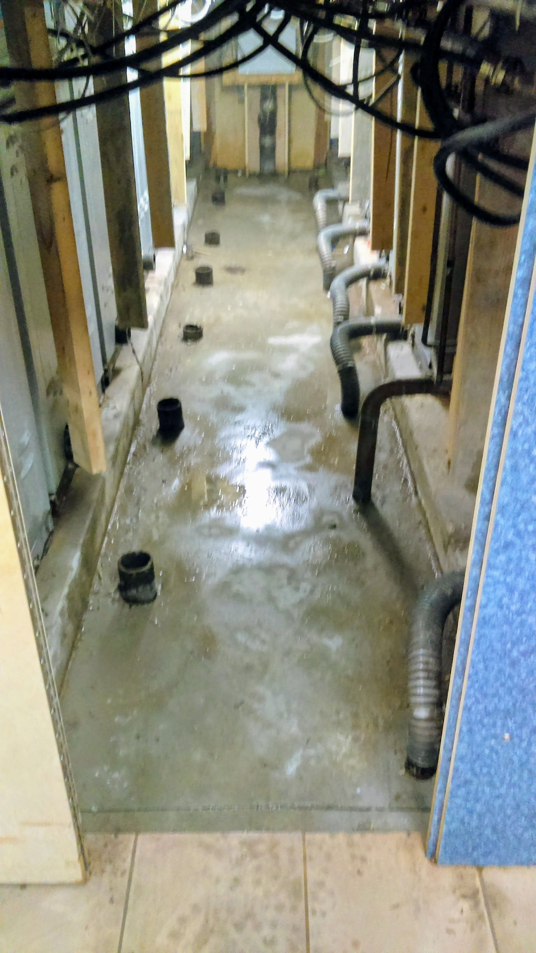 Concrete floor with pipes and conduits in a narrow, industrial setting.