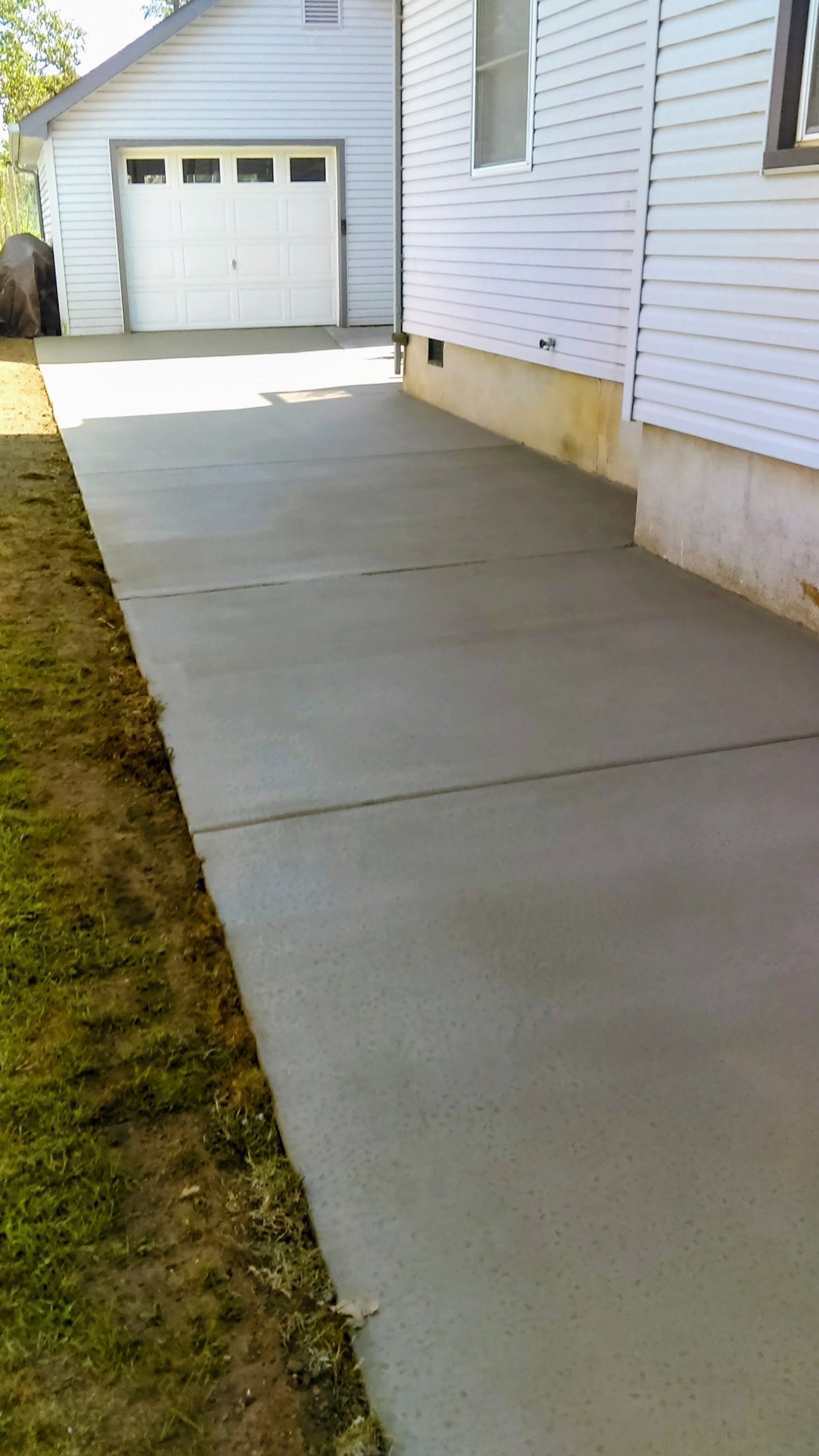Newly poured concrete driveway next to a light-colored house and garage.