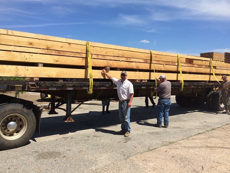 A man is standing in front of a truck loaded with wooden boards