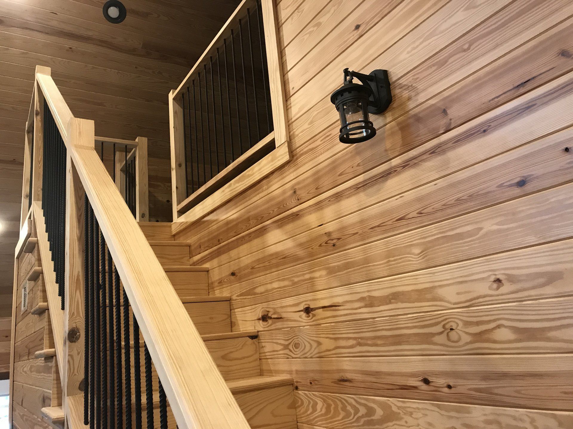 A wooden staircase with a black railing and a light on the wall.