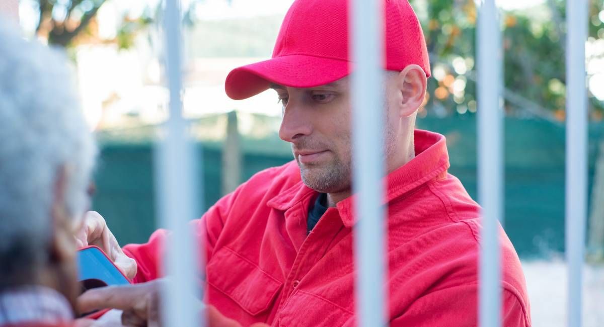 Delivery person in a red cap and jacket looking at a phone to confirm he is at the right address 