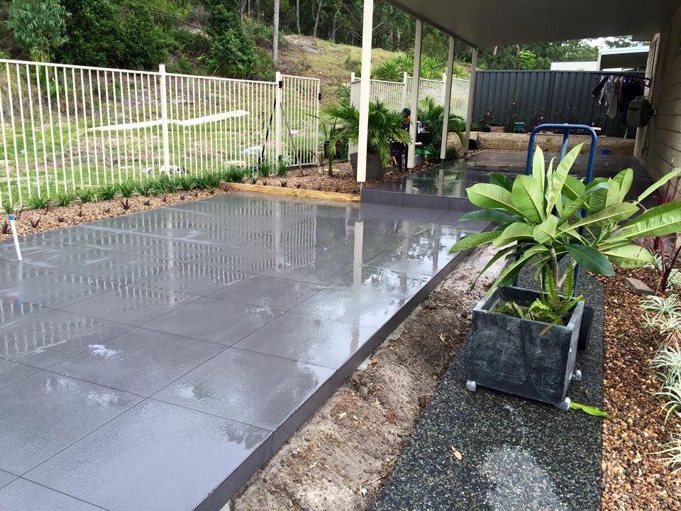 Wet Gray Tiled Patio Next to a Garden Bed and Fence — JNR Building And Maintenance in Green Hill, QLD