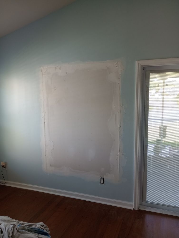 A light blue interior wall featuring a recently patched and sanded drywall section, situated next to a glass door.