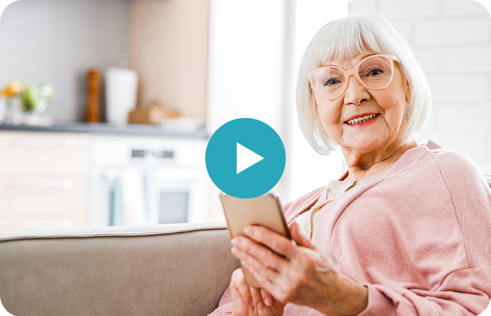 An elderly woman is sitting on a couch using a phone.