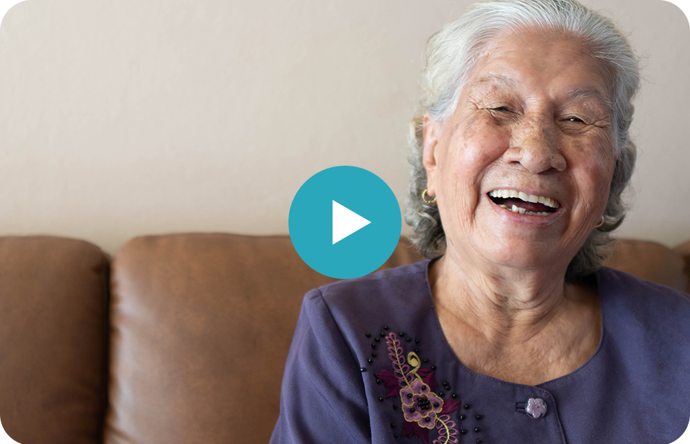 An elderly woman is sitting on a couch and smiling.