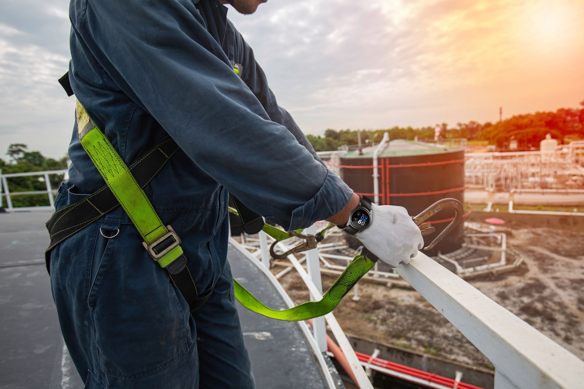 A worker in a blue jumpsuit wearing a safety harness attached to a rail on a roof.