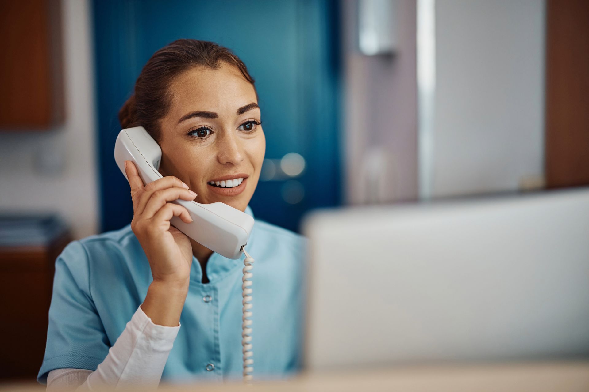 A woman is talking on a telephone while looking at a laptop.