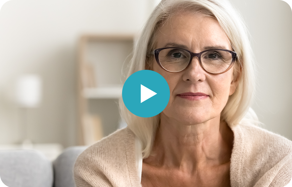An older woman wearing glasses is sitting on a couch.