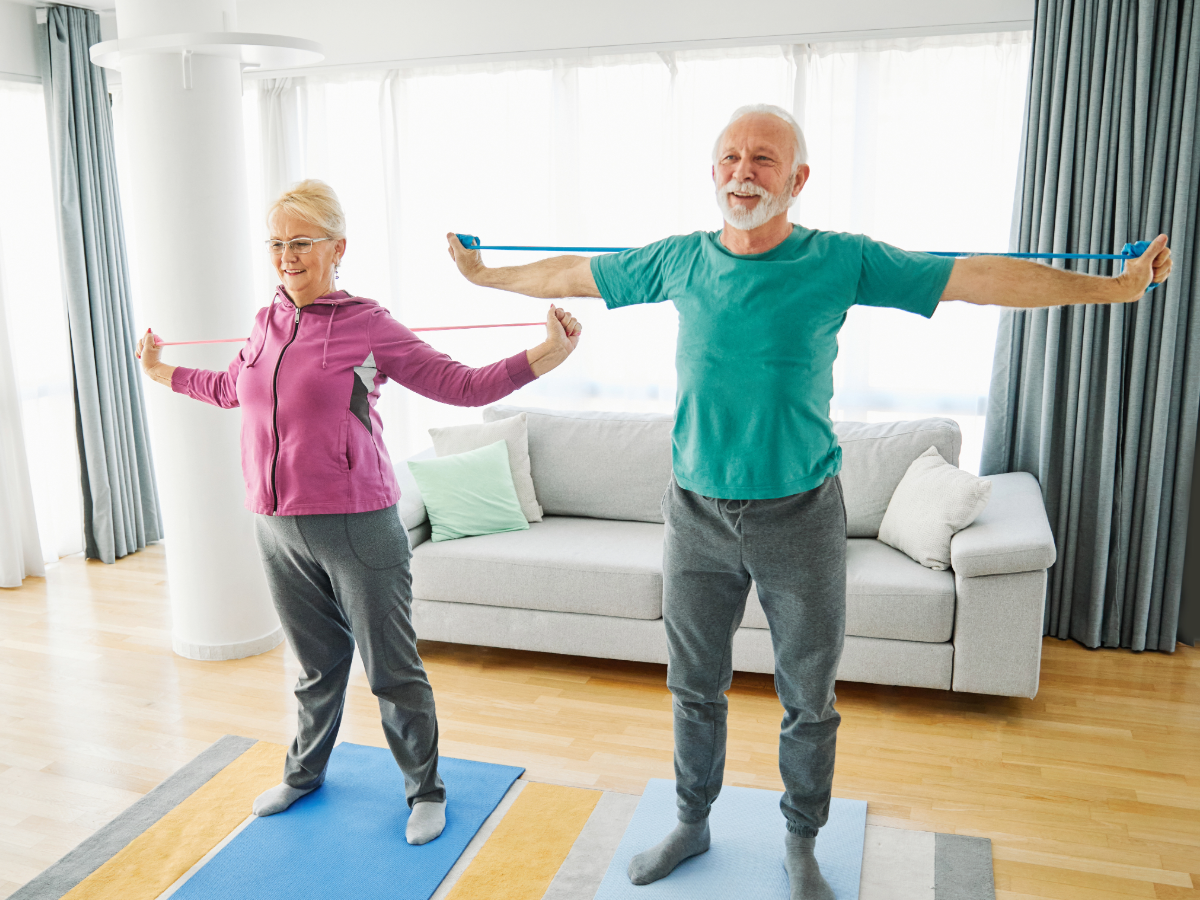 Older couple doing strength and balance exercises with resistance bands at home