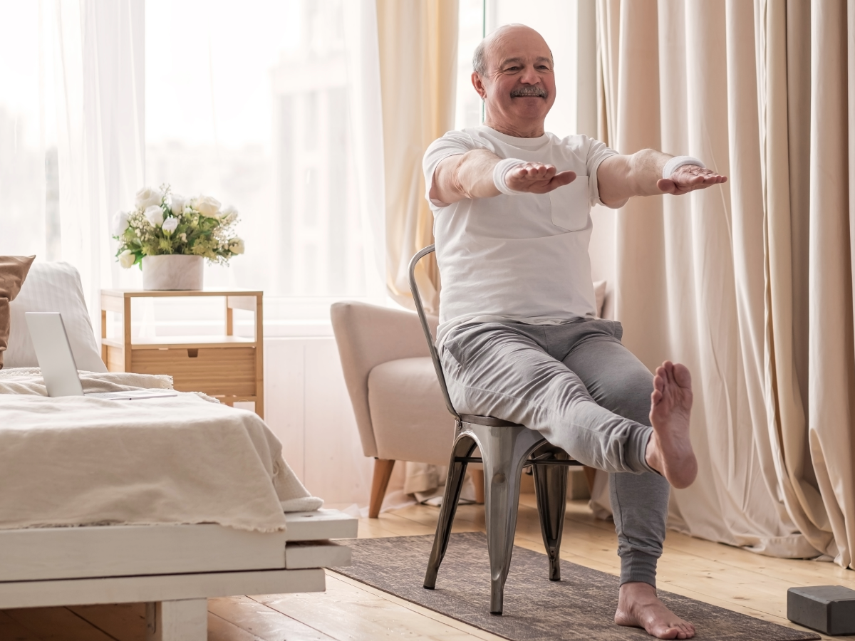 Older man performing seated balance and leg exercises at home