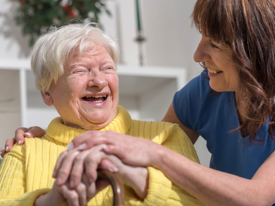 Smiling elderly woman in yellow sweater talking with a caregiver in blue representing support for Carers