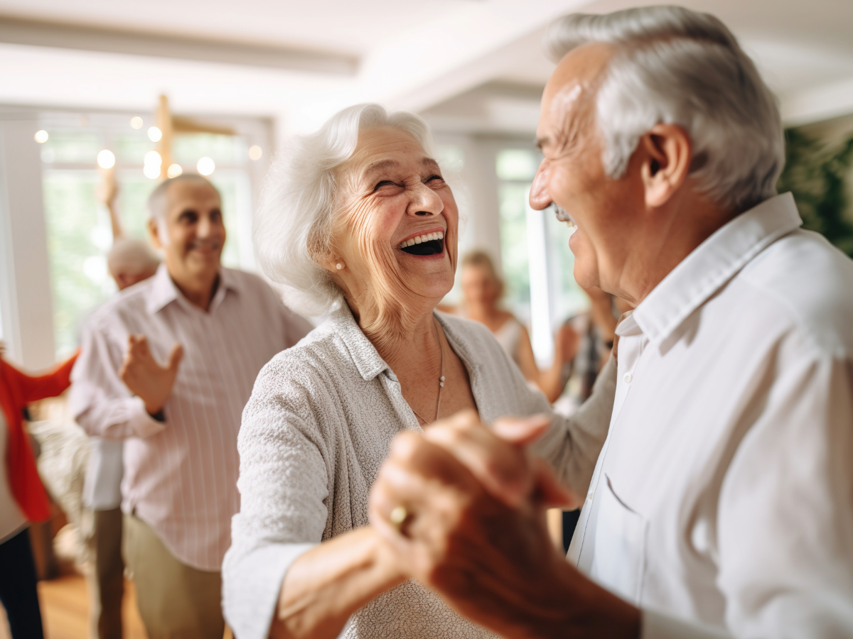 Smiling seniors dancing together at a bright indoor gathering representing support for Retirement Villages