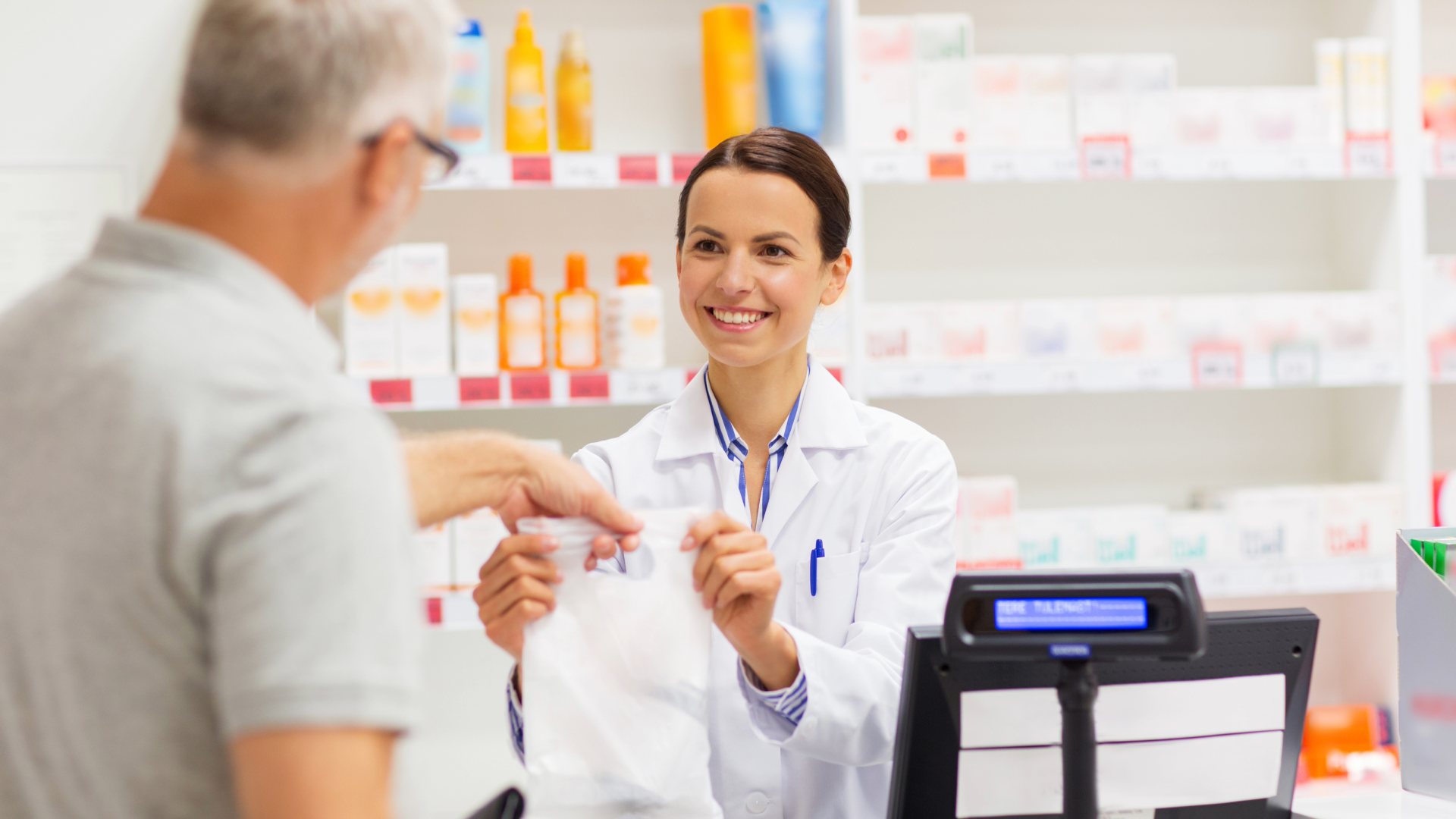 Pharmacist handing a prescription bag to an older man at a pharmacy counter
