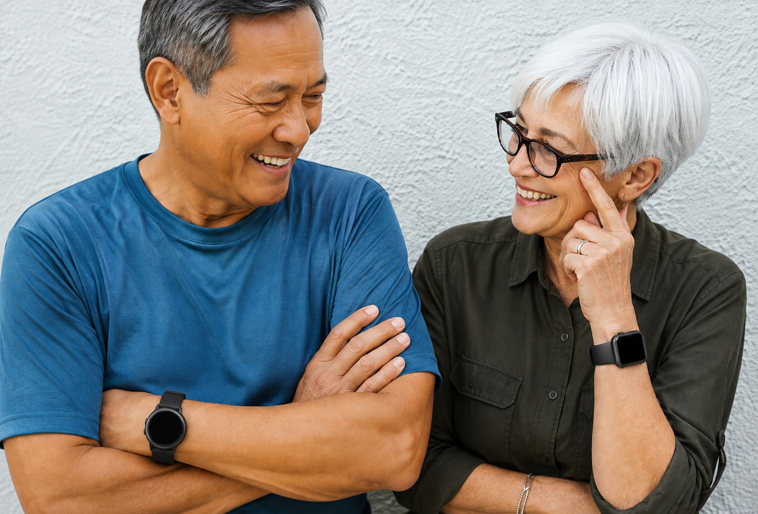 Older man and woman smiling together while wearing smartwatches that can support personal safety and wellbeing monitoring.