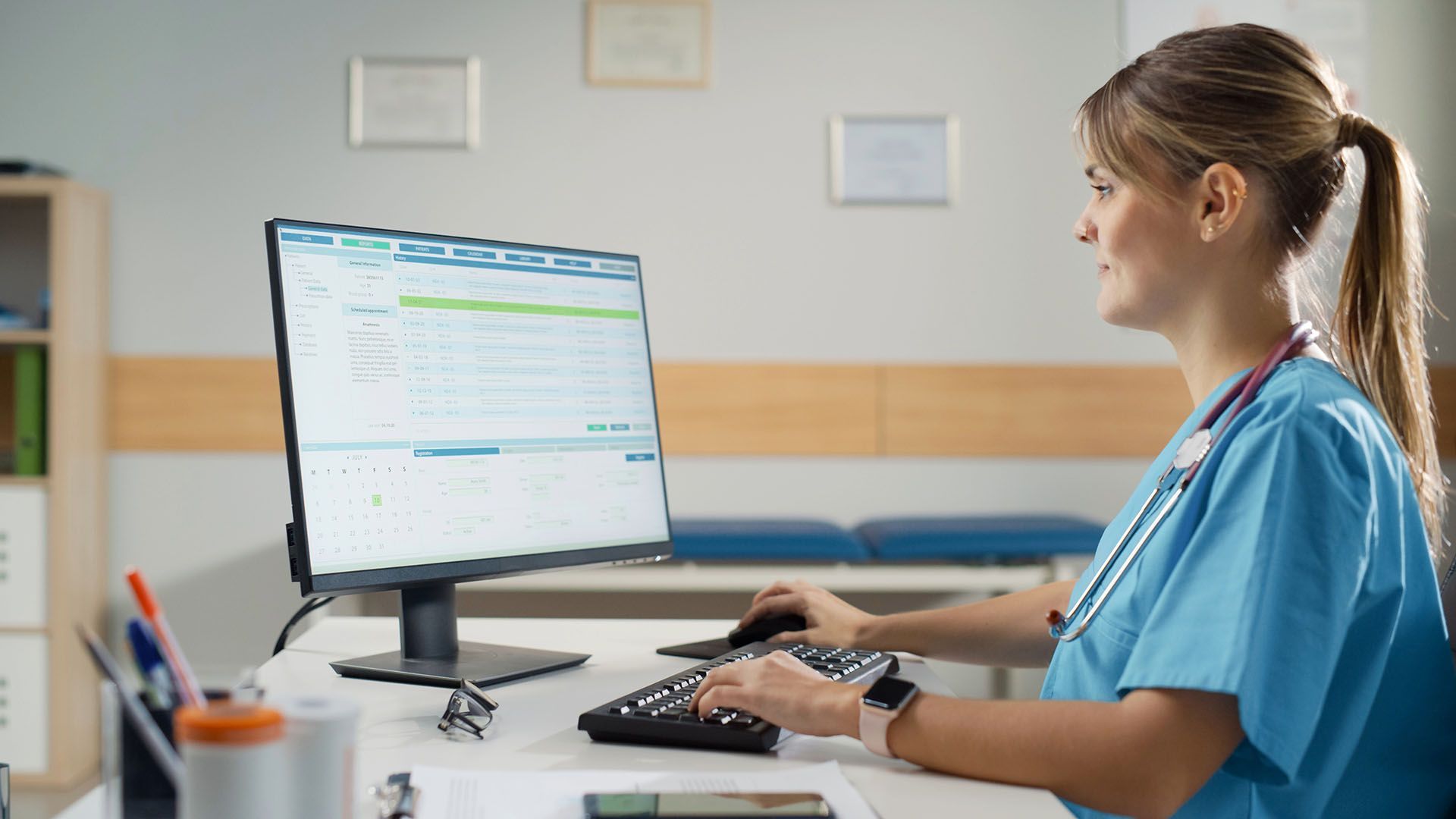 A nurse is sitting at a desk in front of a computer.
