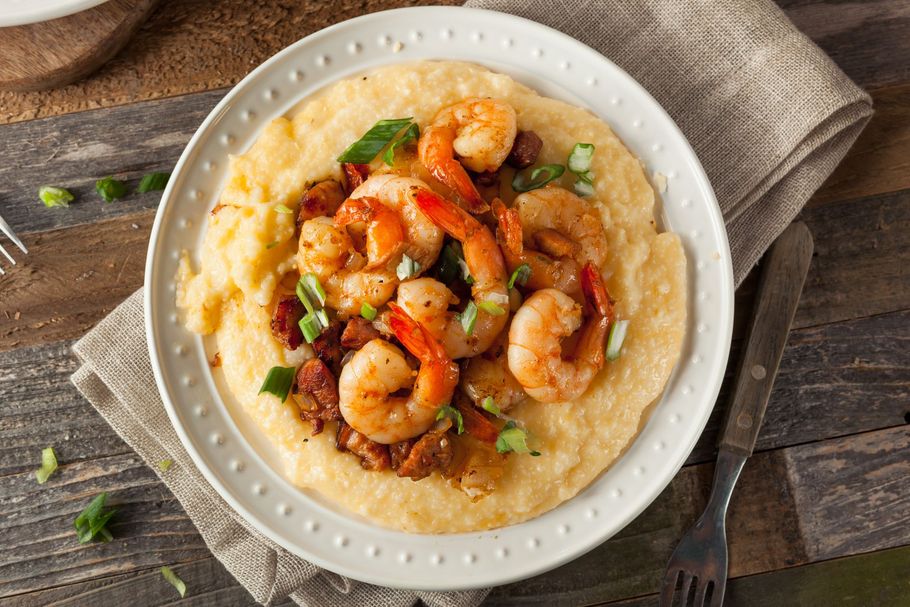 Shrimp and grits topped with sauce and herbs on a white plate
