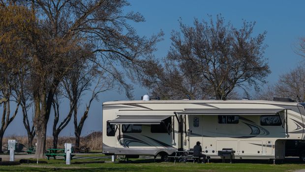 White RV parked on a grassy campsite with leafless trees under a clear blue sky.