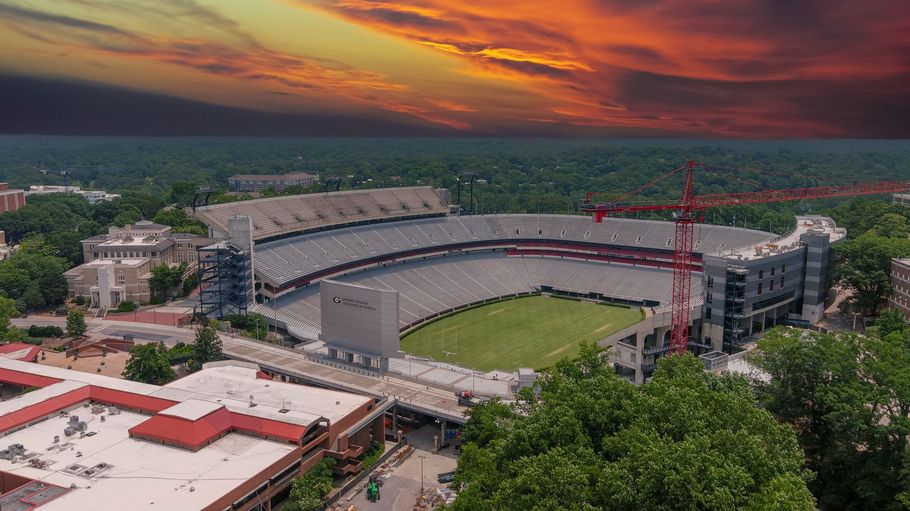 Large stadium with a green field at sunset, surrounded by trees and city buildings.