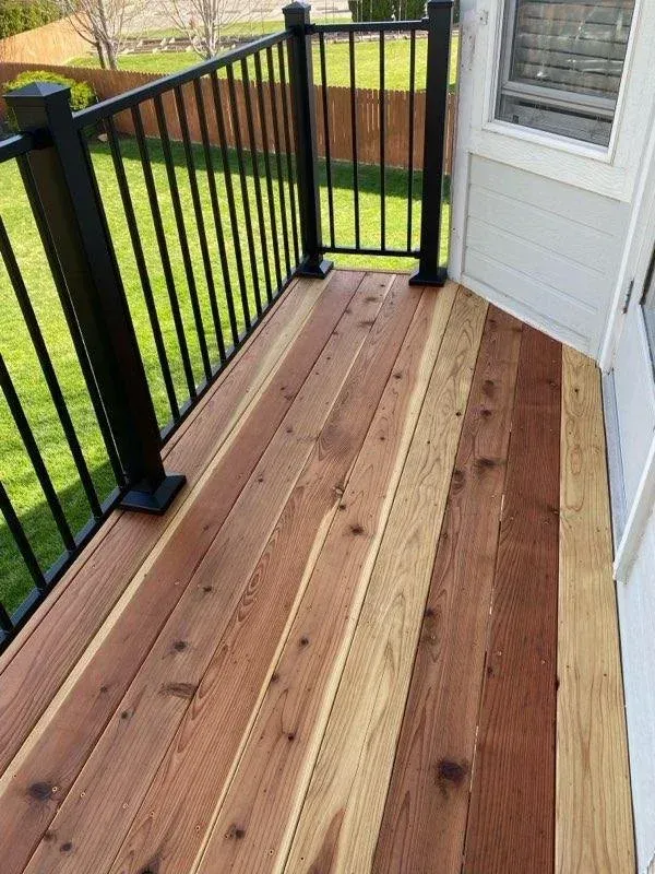 Small wooden deck with black railings beside a house, overlooking a grassy yard.