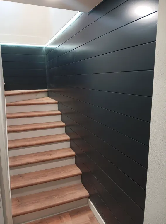 Modern stairway with light wood steps, dark wall paneling, and recessed ceiling lighting