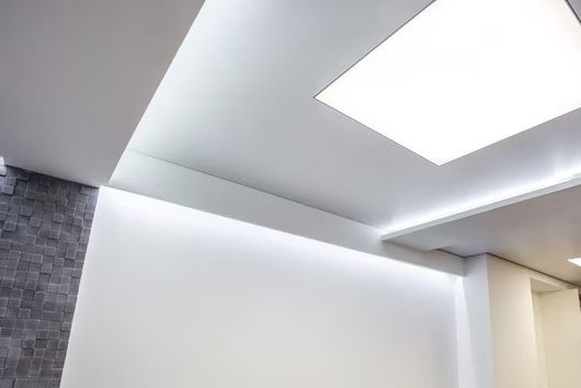 Modern interior ceiling with recessed lighting and a bright skylight above a white wall
