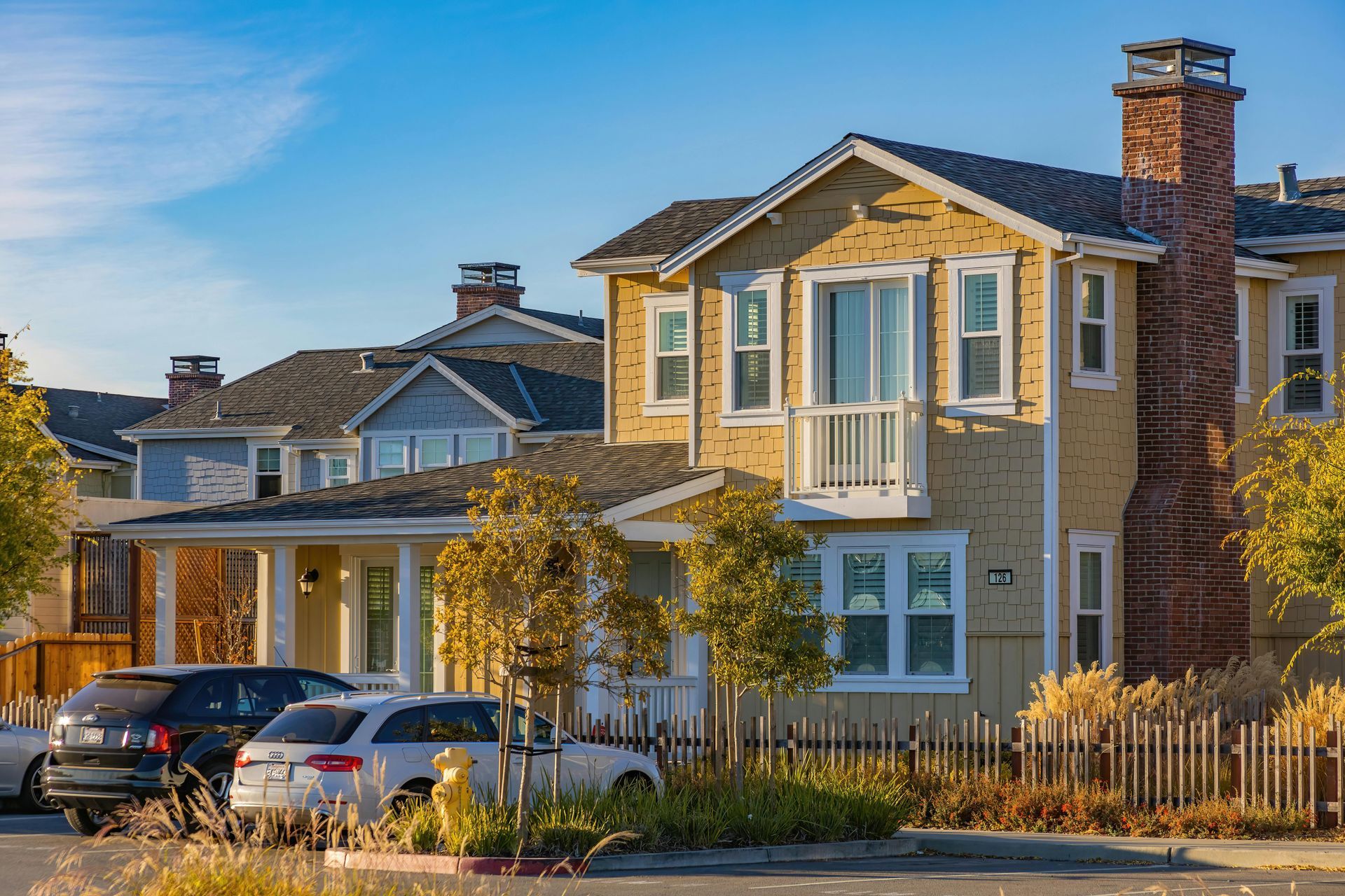 Suburban houses with parked cars in front, lit by warm sunlight.