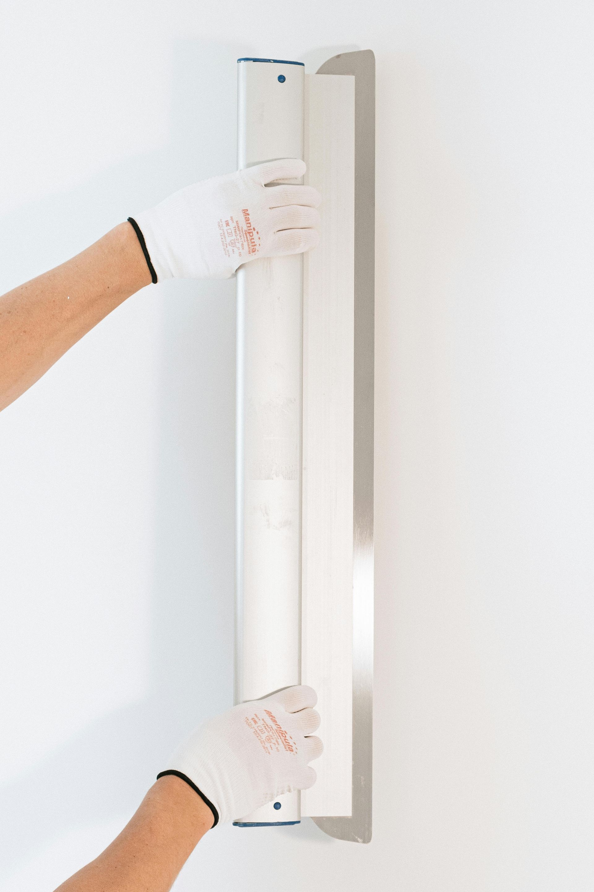 Hands holding a vertical white wall-mounted bar against a light wall.