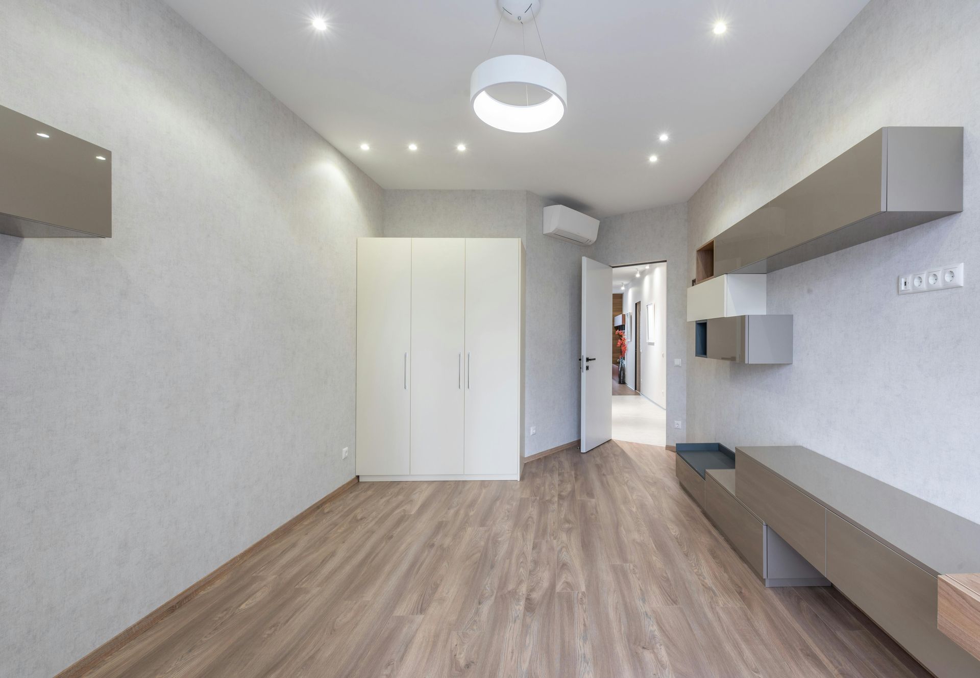 Bright empty modern room with wood floor, white walls, built-in cabinets, and ceiling lights