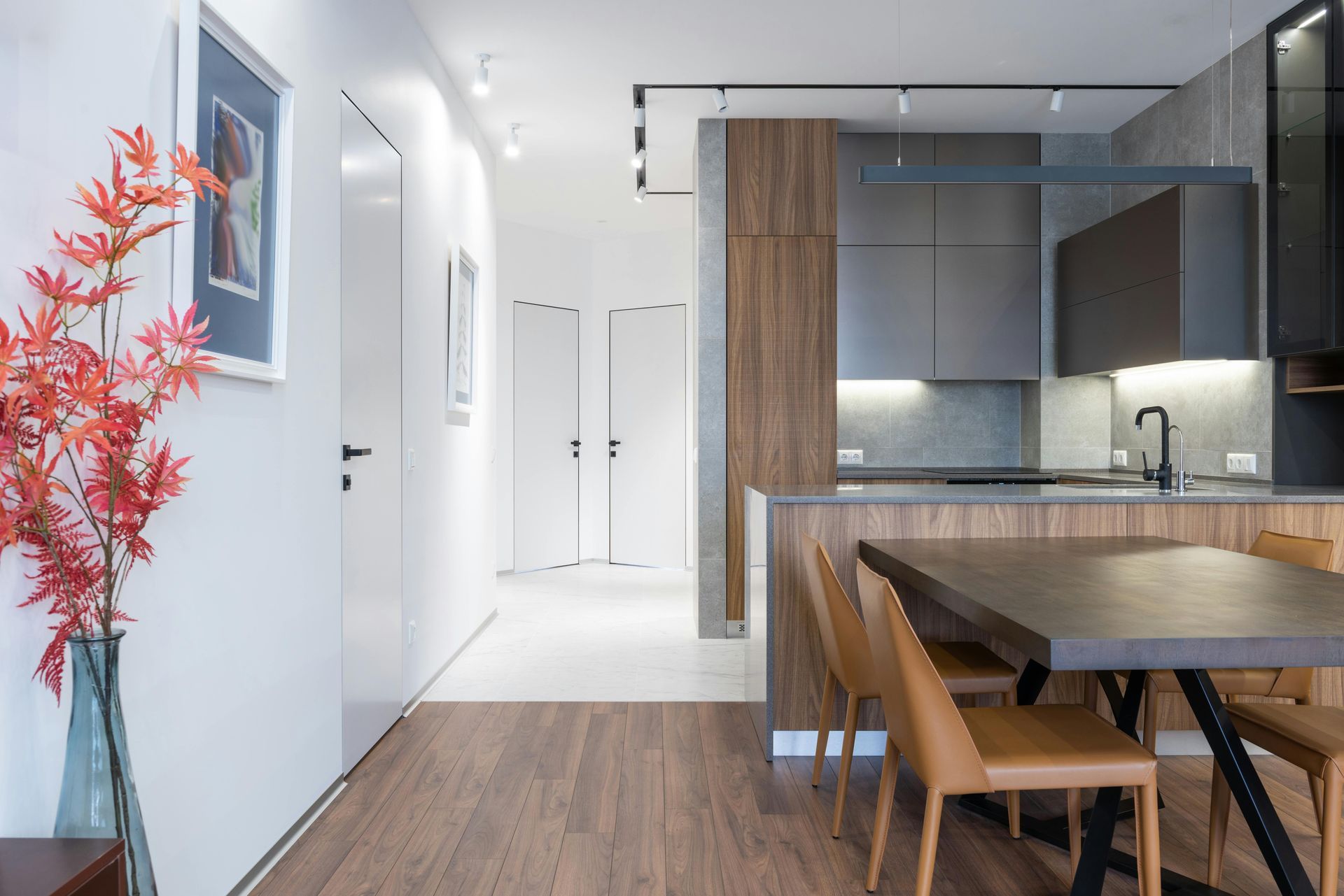 Modern apartment kitchen and dining area with wood floors, white hall, and red decorative plant