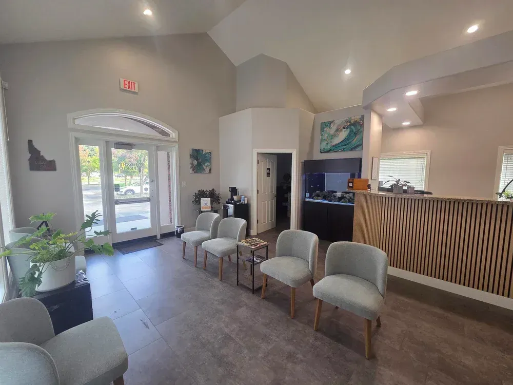Modern lobby with arched glass entrance, gray chairs, wood reception desk, and potted plants.