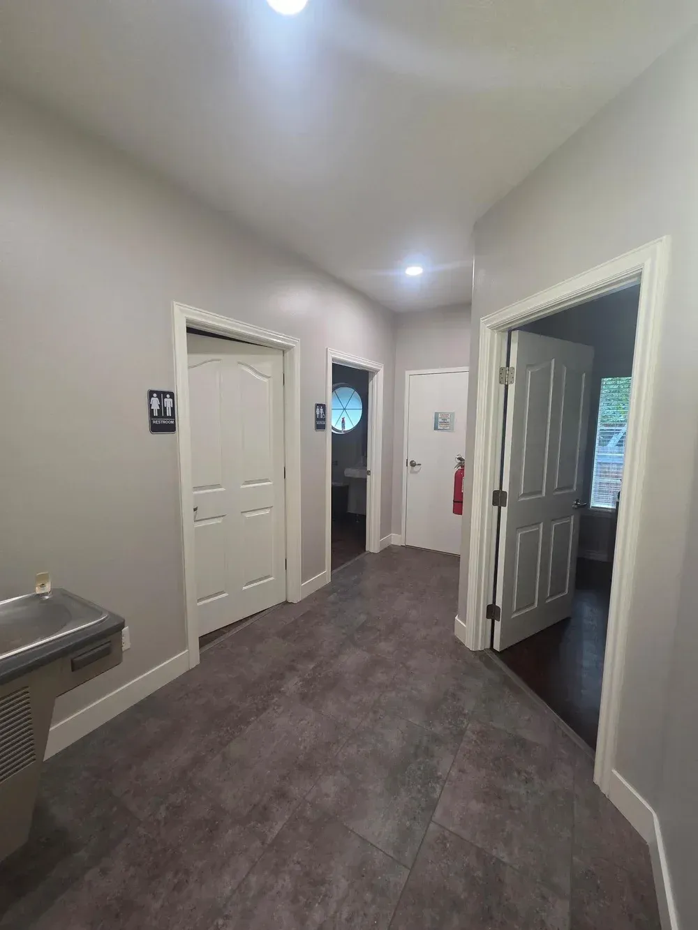 Empty apartment hallway with gray carpet, white doors, and a water fountain on the left