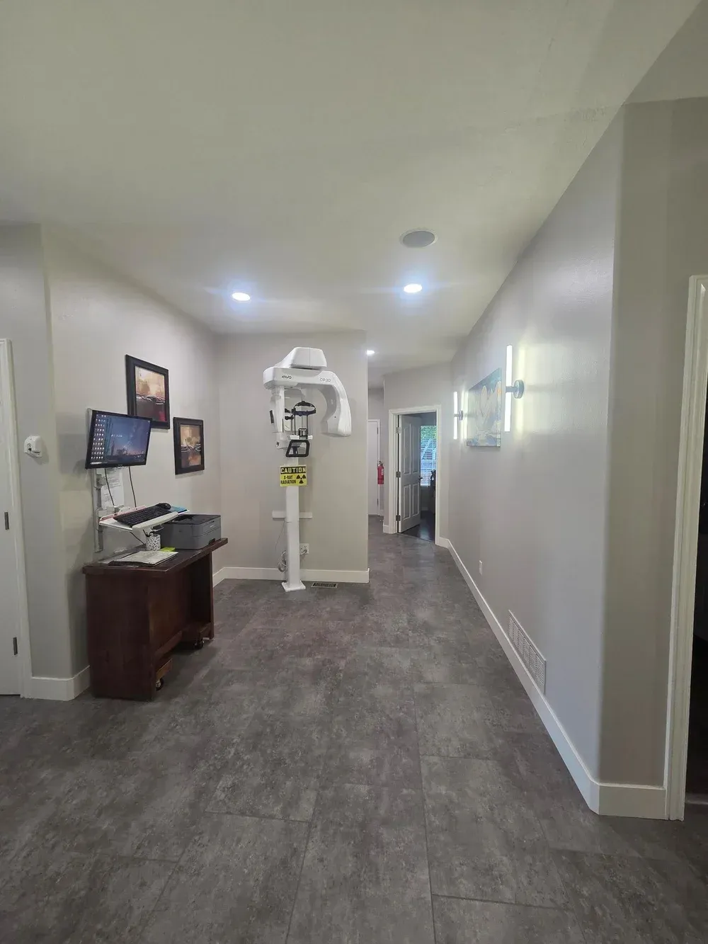 Bright hallway with gray carpet, white walls, and a medical imaging machine at the end.