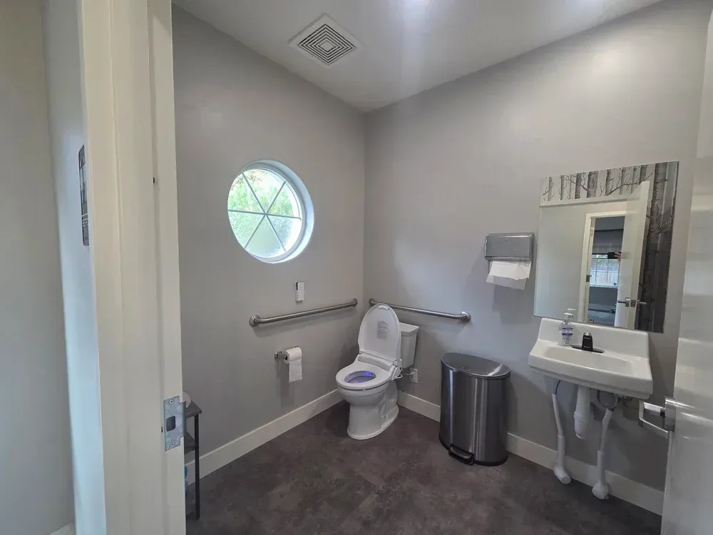 Accessible bathroom with toilet, sink, mirror, grab bars, and circular window