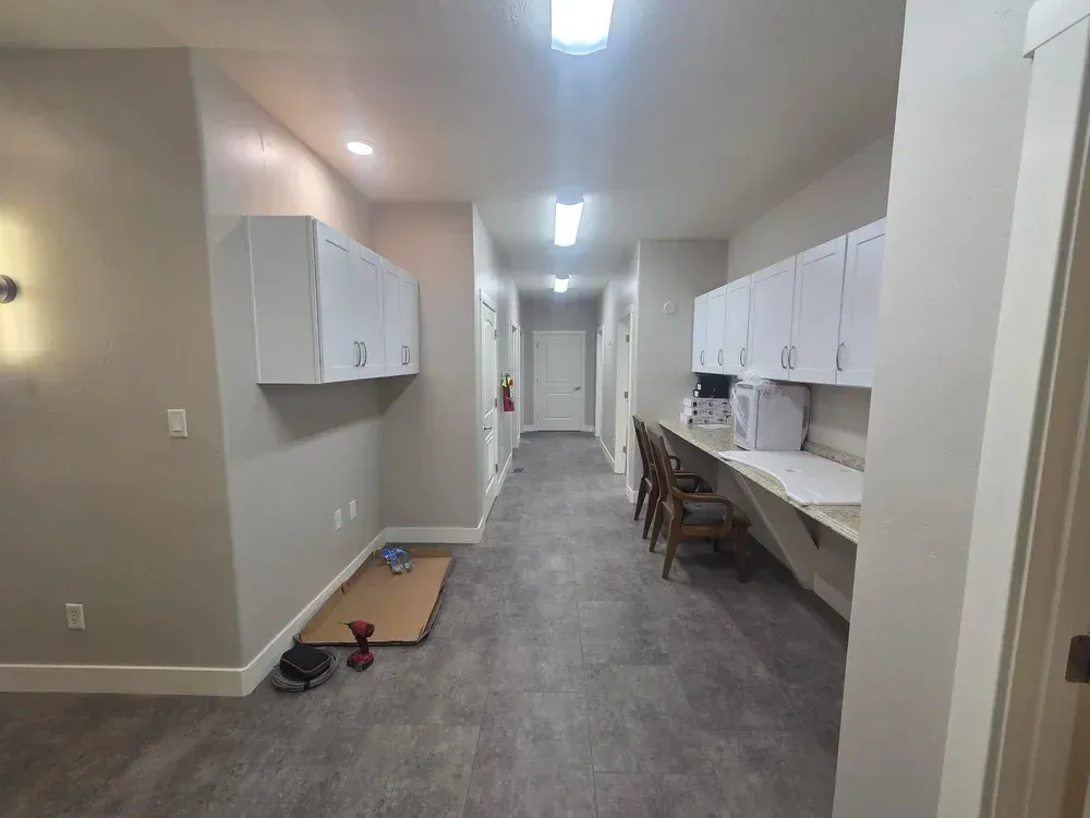 Long hallway with white cabinets, desks, and gray carpet in a building interior