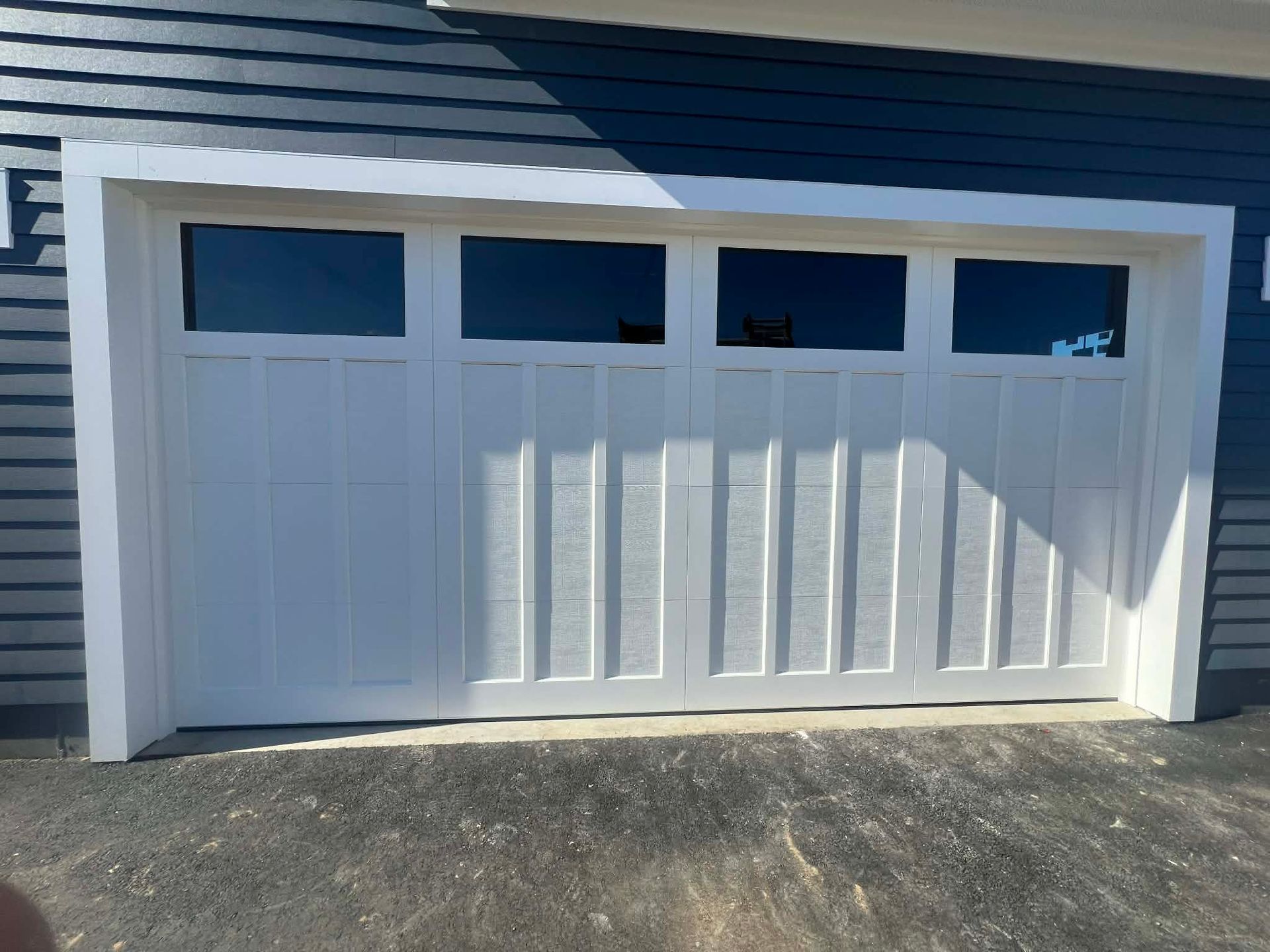 White garage door with four top windows and white trim against a blue house.