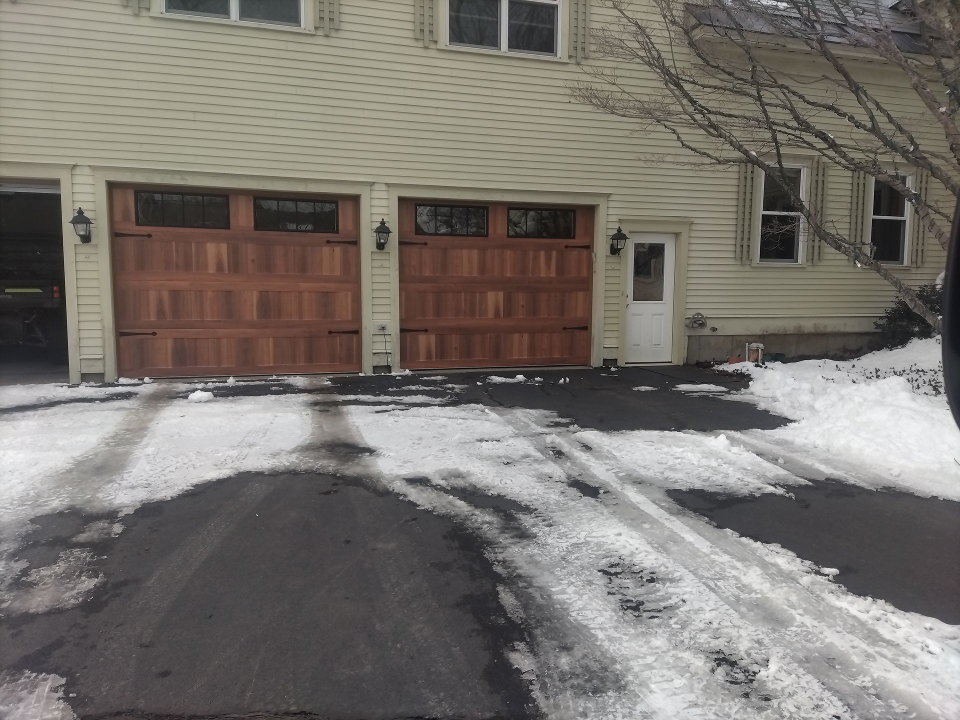 Brown wooden garage doors on a light-colored house; snowy driveway.
